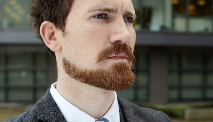 Ginger man wearing beanie hat with moustache and beard shaped into a downward point at the chin.
